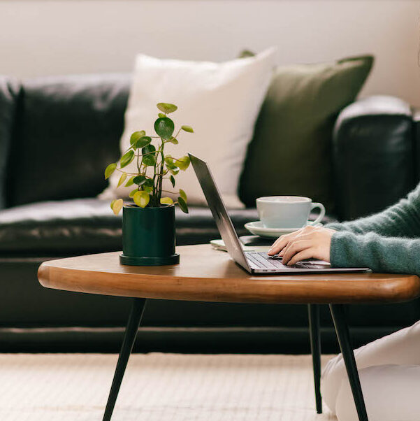Side shot of hands typing on a laptop on a coffee table with a mug and plant.