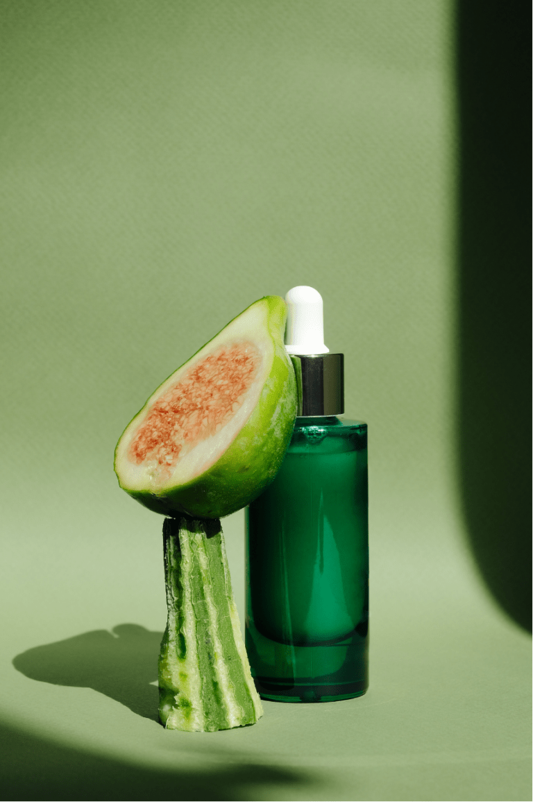 A green-tinted glass serum bottle and a slice of guava