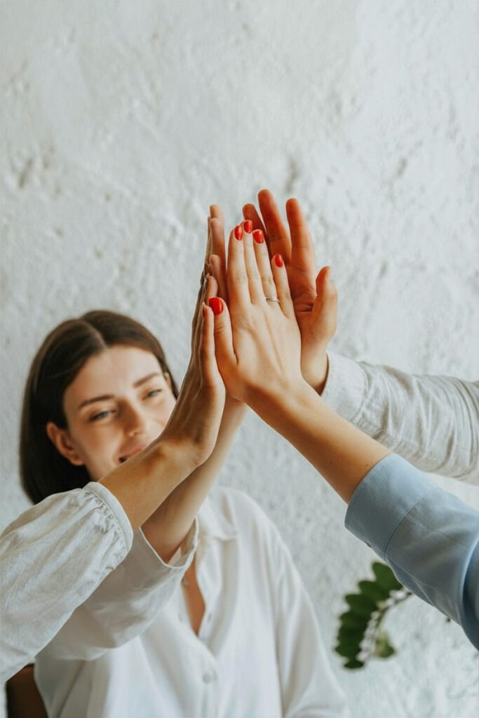Group of people giving a high-five symbolizing teamwork and cooperation with a smiling woman in the background.